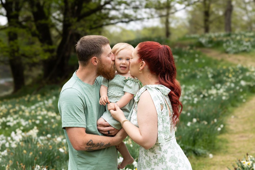 A family shares a tender moment together in a spring meadow filled with blooming white wildflowers.