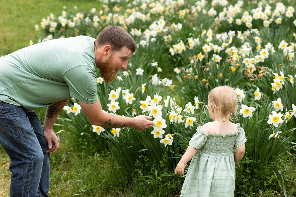 Two people looking at blooming daffodils in a spring garden, with one pointing at the yellow and white flowers.