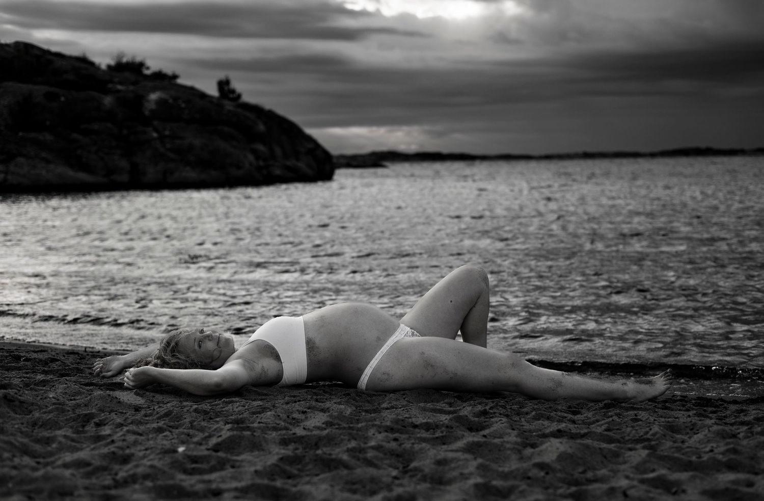 gravid kvinna ligger ned på stranden vid havskanten. bilden är i svartvit.