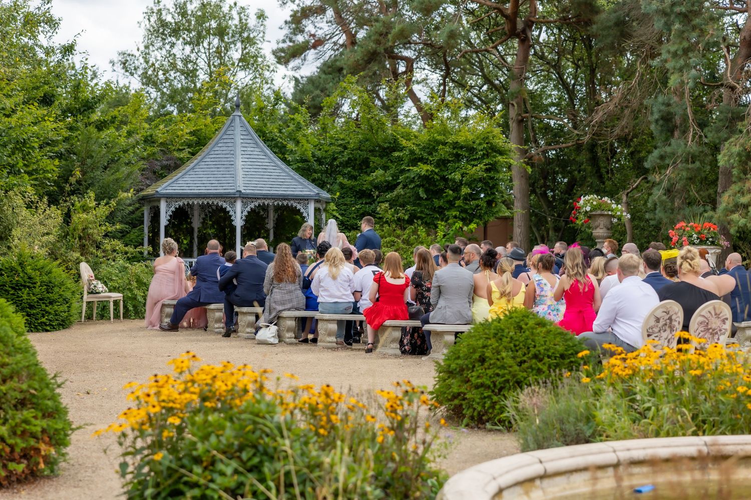 A couple stands under a white umbrella at an elegant entrance with stone pillars and floral arrangements. Bowburn Hall Wedding Durham