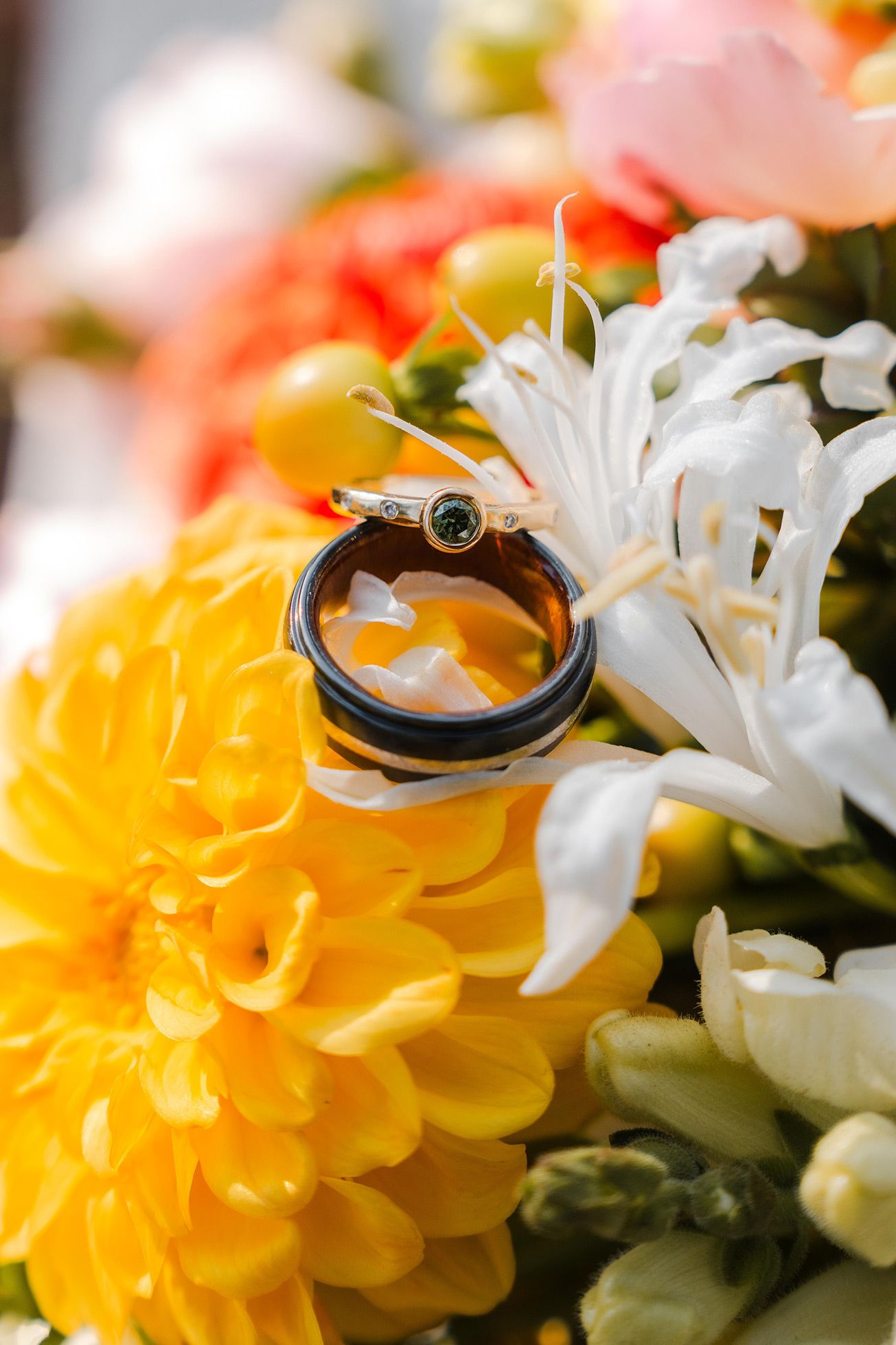 Two wedding rings resting on yellow and white flowers in a colorful bridal bouquet.