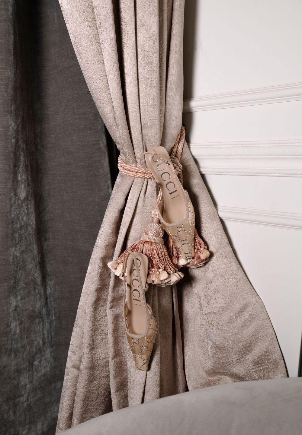 Beige linen curtain tie-back with decorative ceramic holder mounted on white wall creates elegant window treatment.