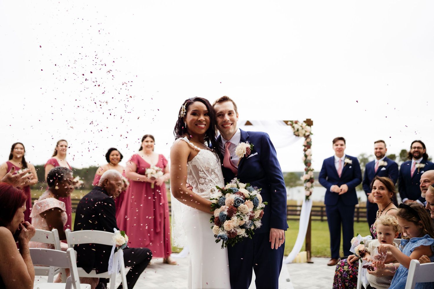 Wedding guests celebrate by tossing confetti and rice at the happy couple during an outdoor ceremony.