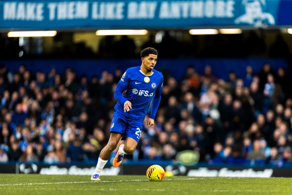 A soccer player in a blue jersey dribbles the ball during a match at a packed stadium.