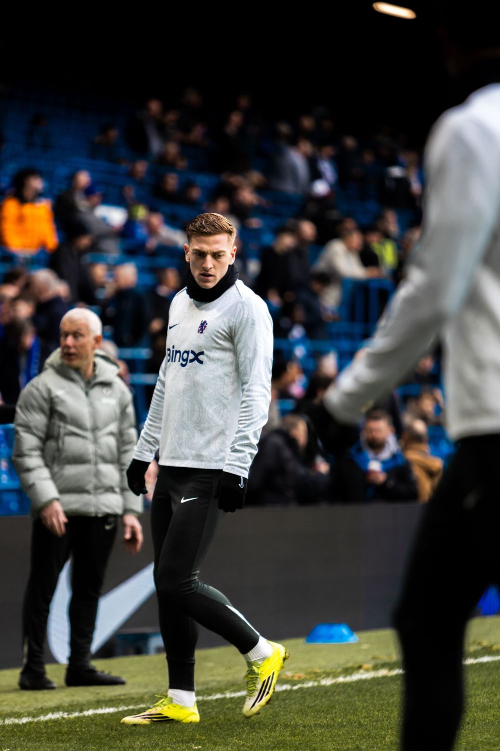 Soccer players warm up on the sideline wearing black and white training gear before a match at a stadium.