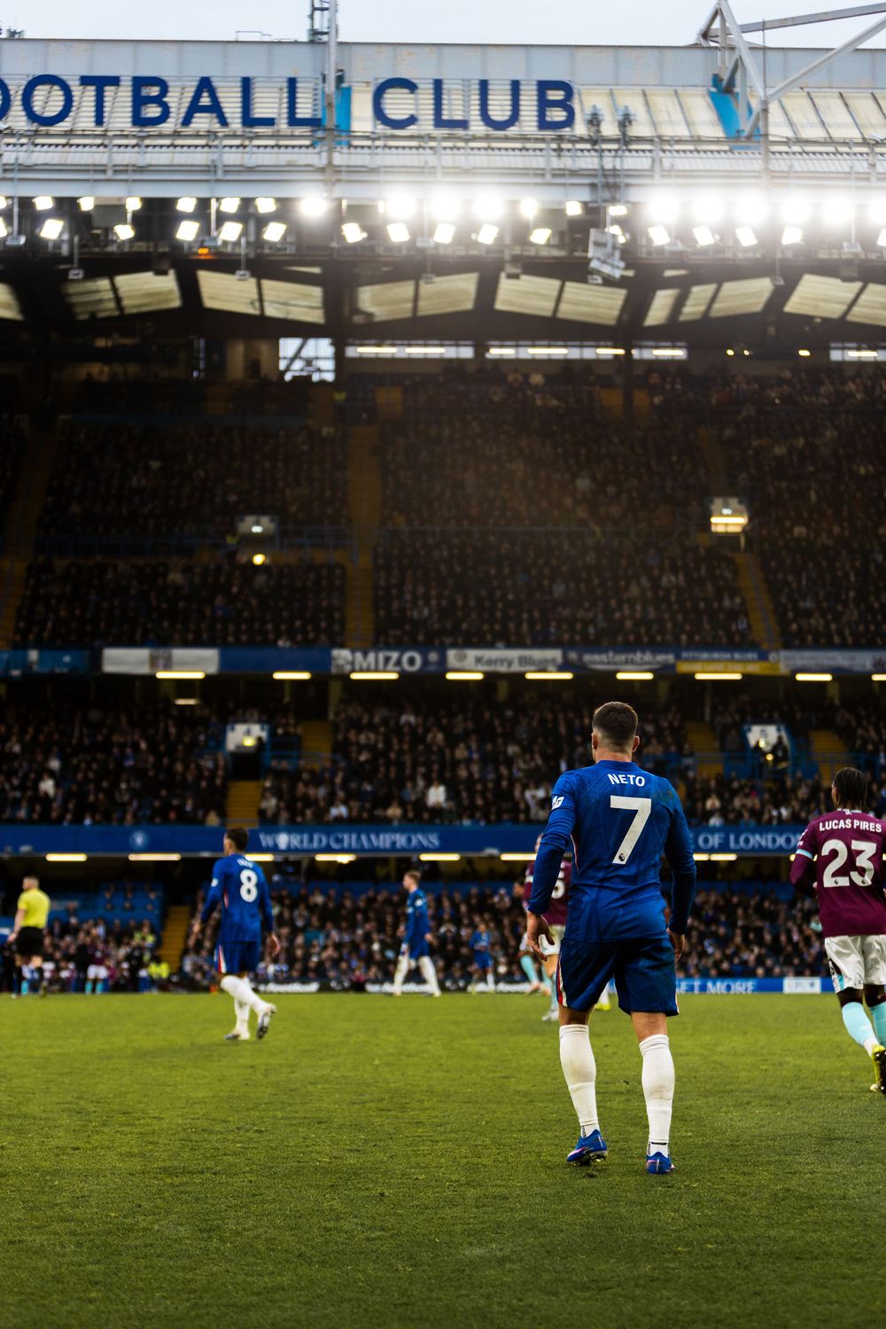 Soccer players in blue uniforms walk across a floodlit stadium field during an evening match at a football club.