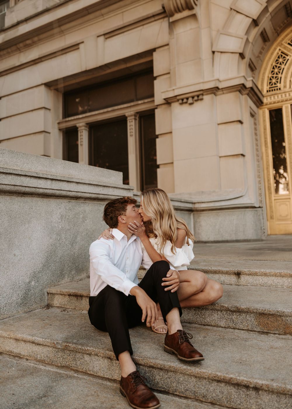 Romantic couple sitting on stone steps of historic building during golden hour.