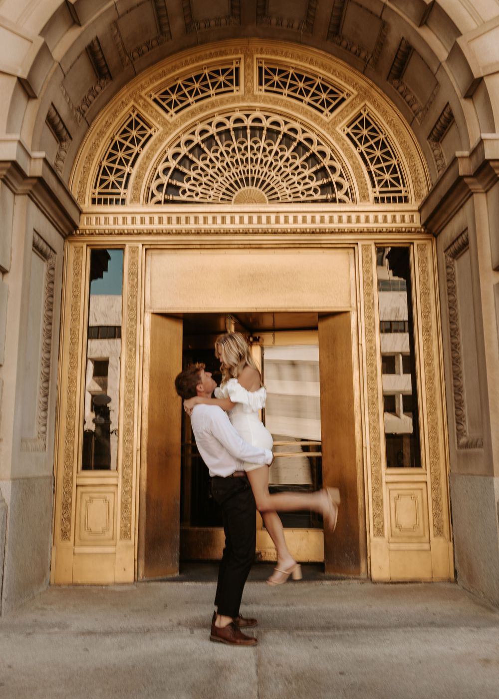 A couple dancing and twirling together in a grand archway with ornate architectural details.