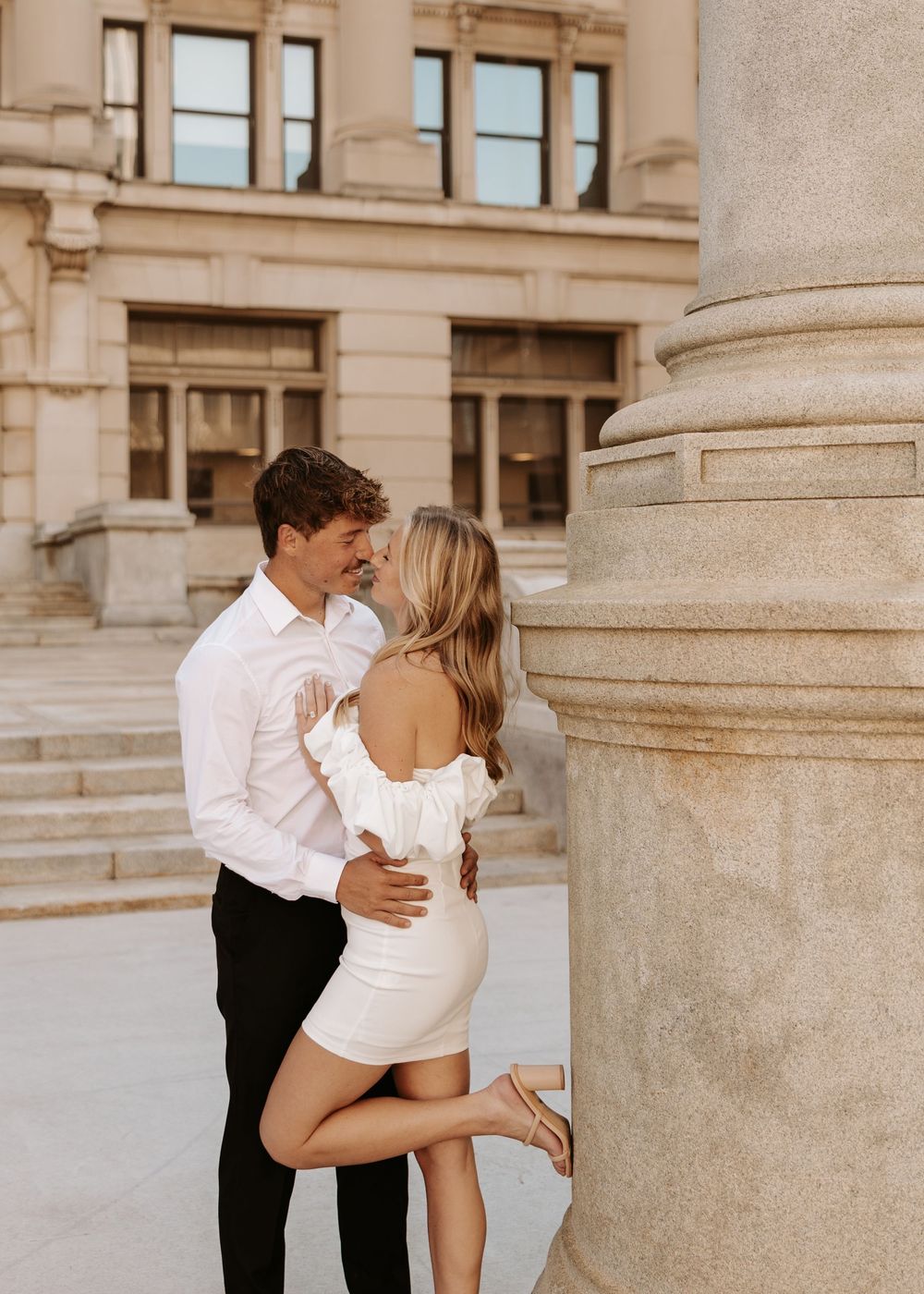 Romantic couple embraces and kisses on elegant stone steps of historic building in sepia tones.