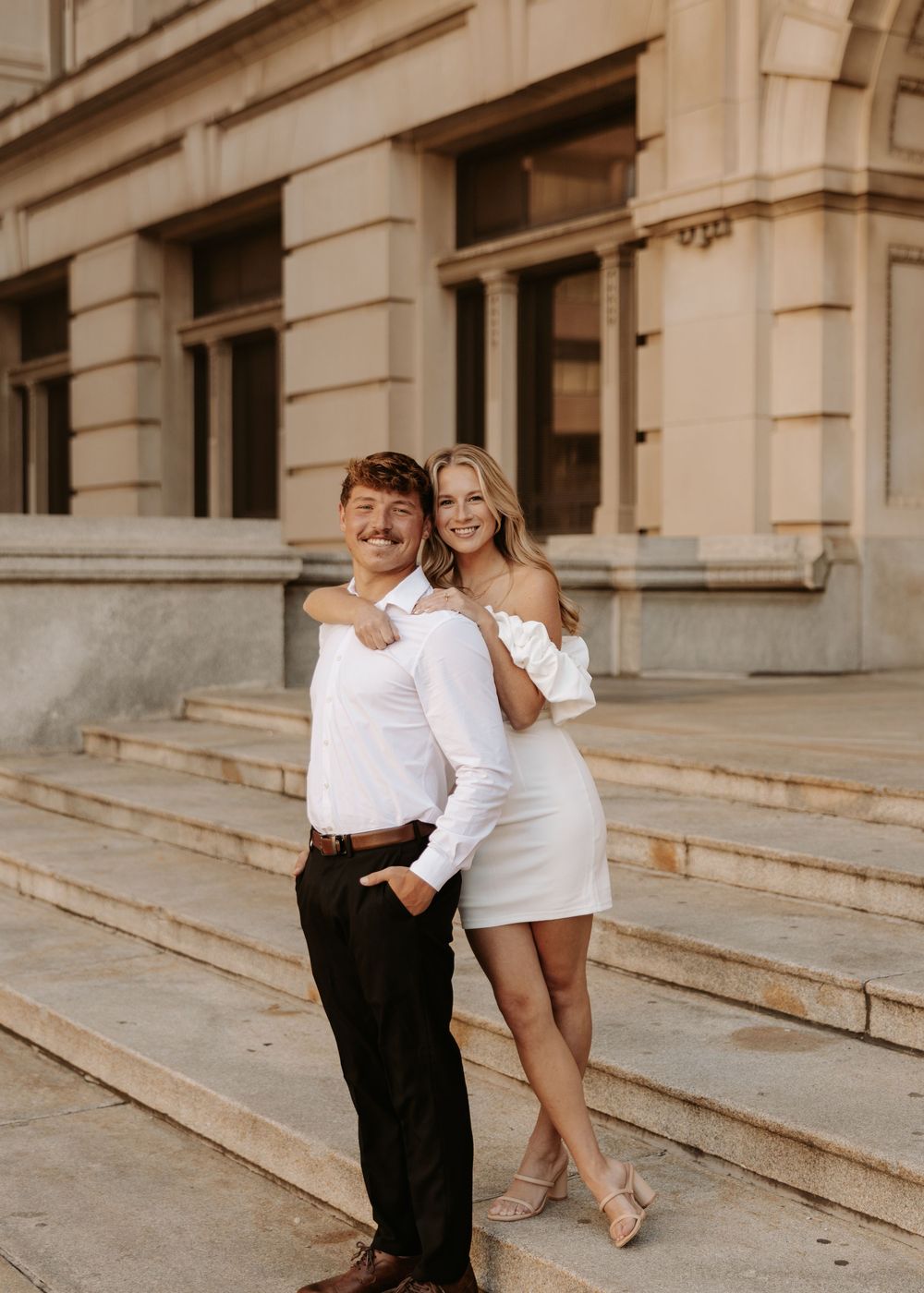 Two people in white outfits share playful moments on stone steps of a grand building in a series of candid shots.