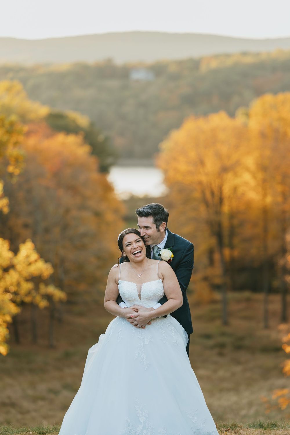 A couple shares a romantic moment in their wedding attire against a backdrop of golden autumn trees at sunset.