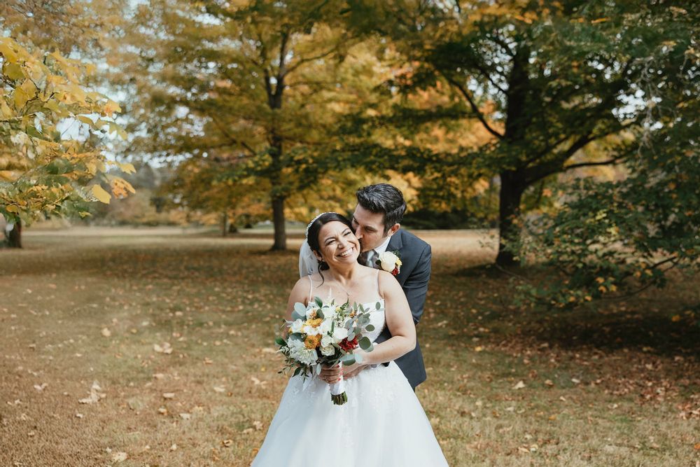 A couple embraces under golden autumn trees during an outdoor wedding photoshoot.