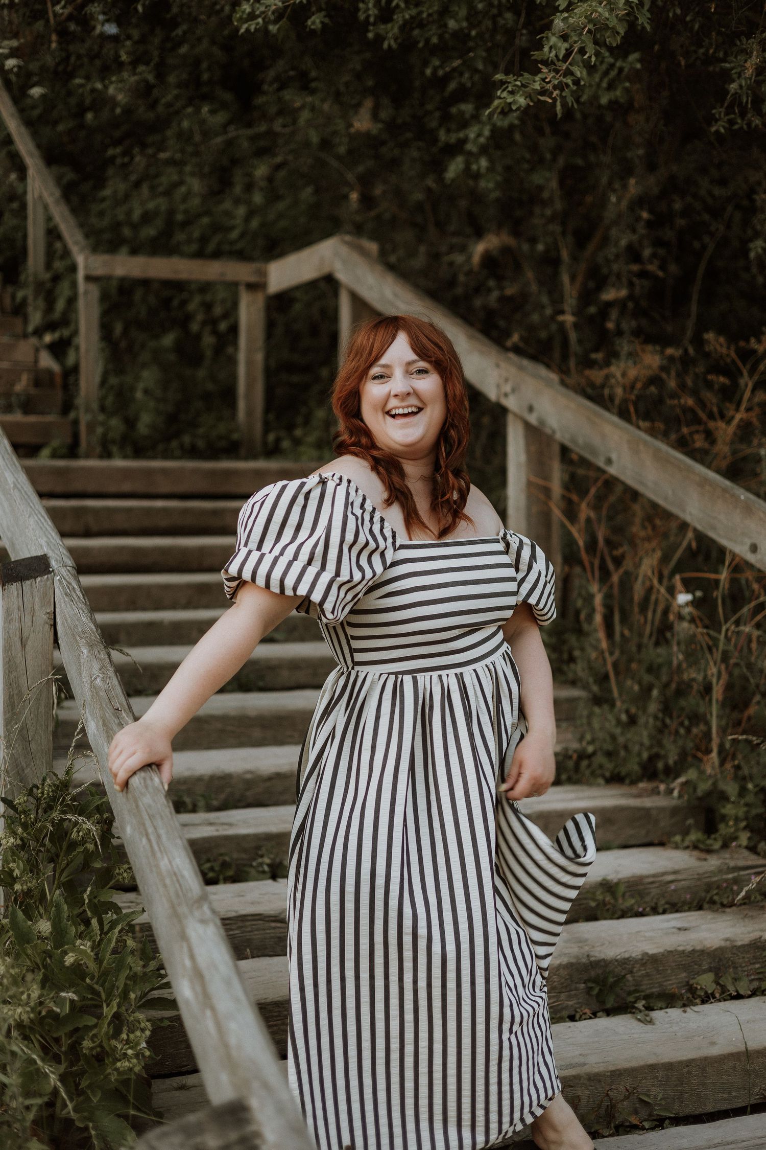 A person in a black and white striped dress poses playfully on wooden steps outdoors during a photo session.