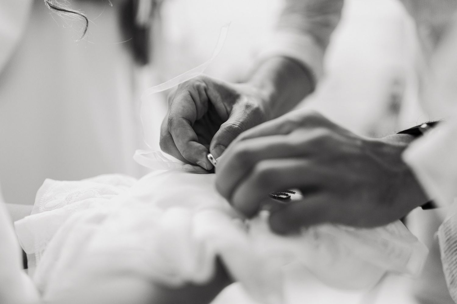 Close-up black and white shot of hands sewing delicate white fabric or garment details.