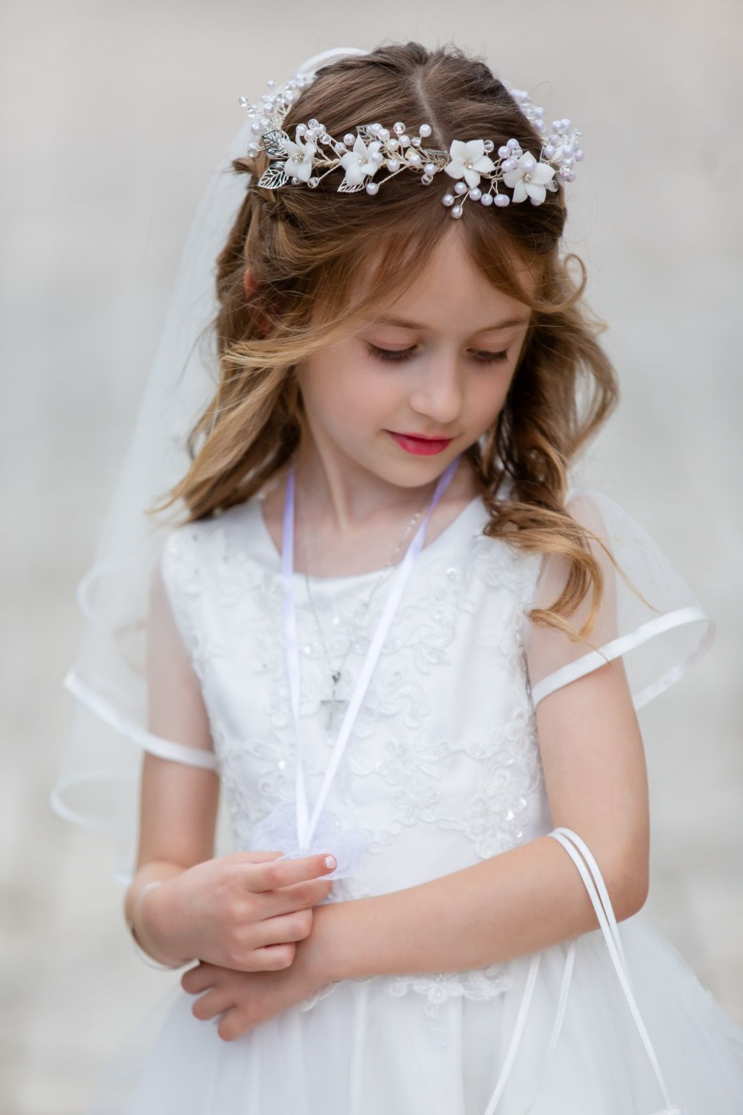 Elegant first communion portrait featuring white dress, floral crown and flowing veil.