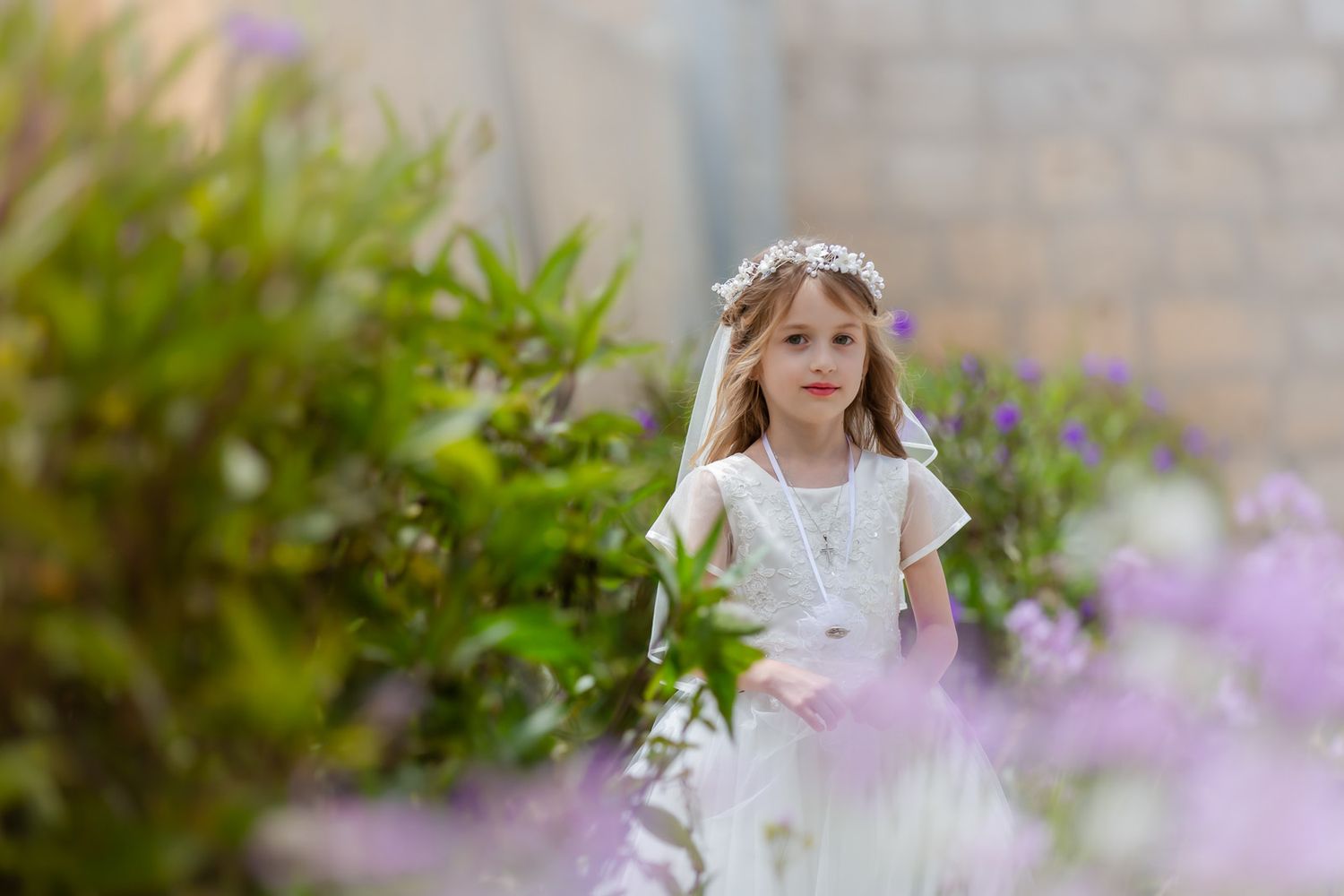 A young girl in a white dress twirls joyfully in a garden with purple flowers and greenery in the background.