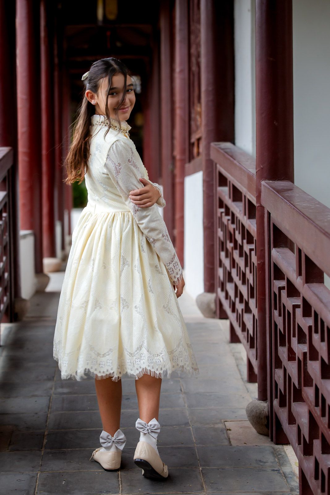 Person in a vintage-style white lace dress and boots poses along a traditional Asian corridor with red pillars.