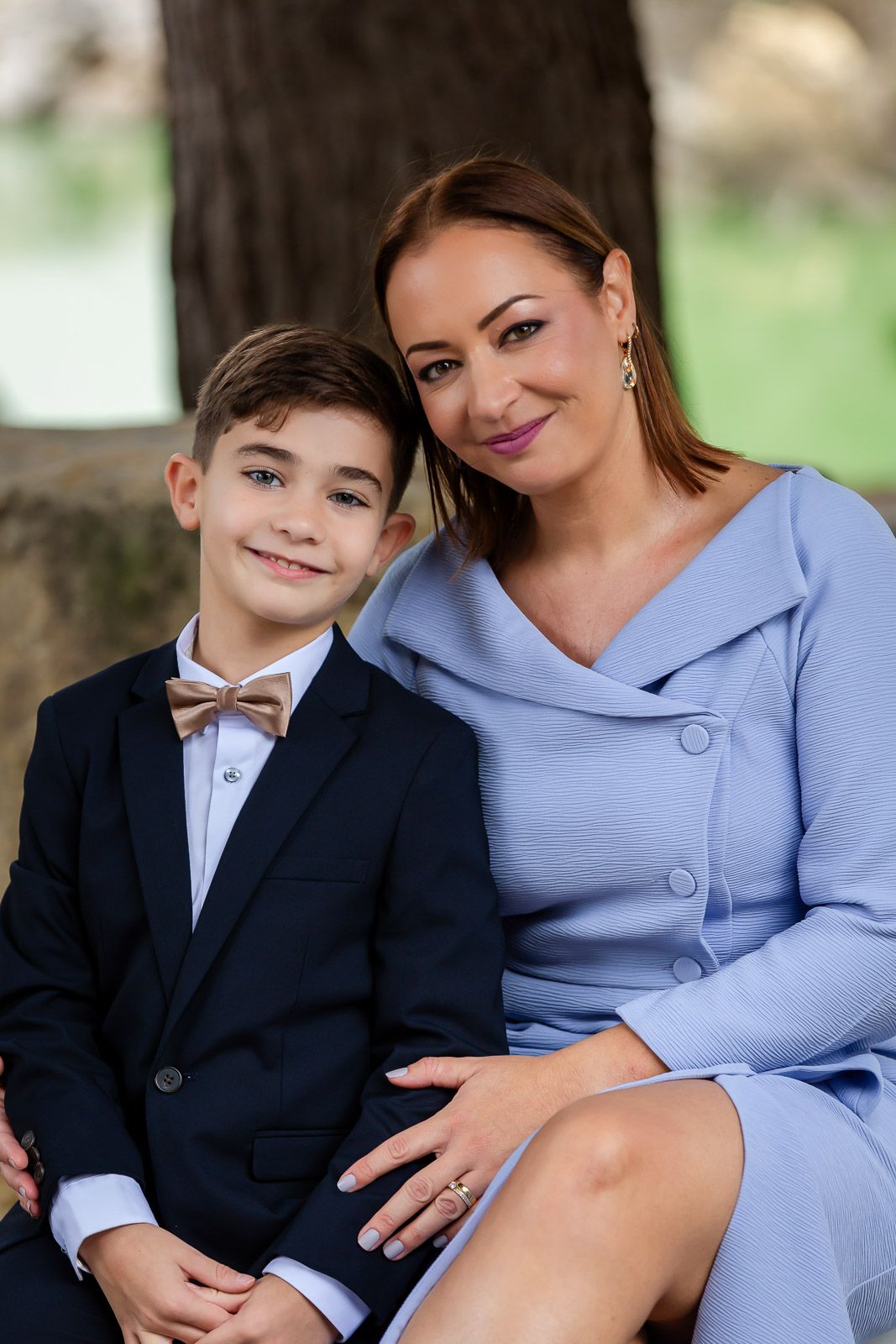 A mother and young boy in formal attire sit together outdoors for a series of intimate portrait photographs.
