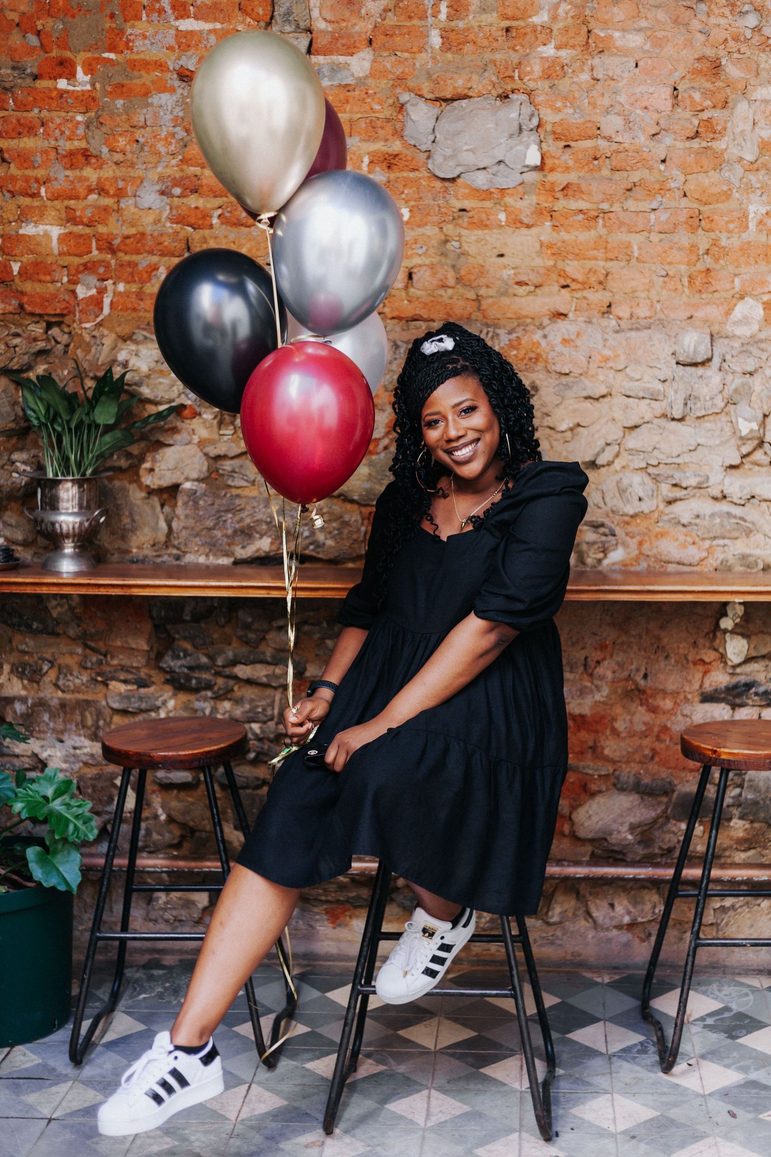 Celebratory scene with balloons against brick wall featuring black dress and white sneakers.