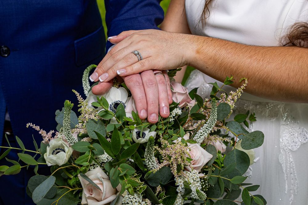 Hands arrange white and green floral stems and eucalyptus leaves into a wedding bouquet on a dark surface.