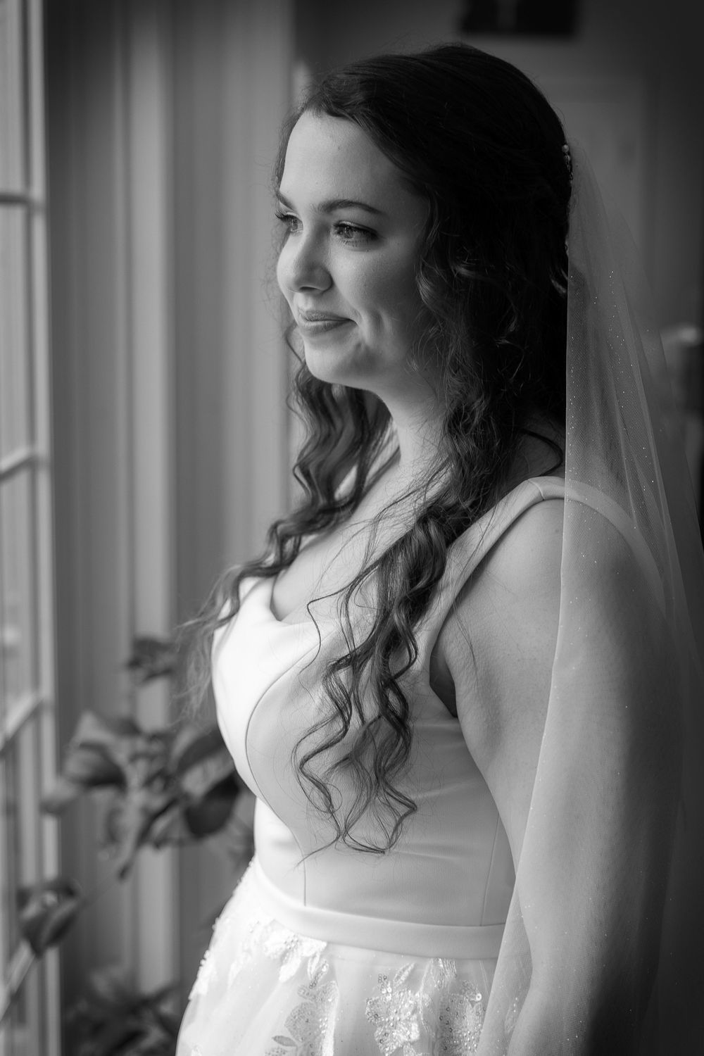 Black and white portrait series of a bride in a white dress standing by a window with natural lighting.