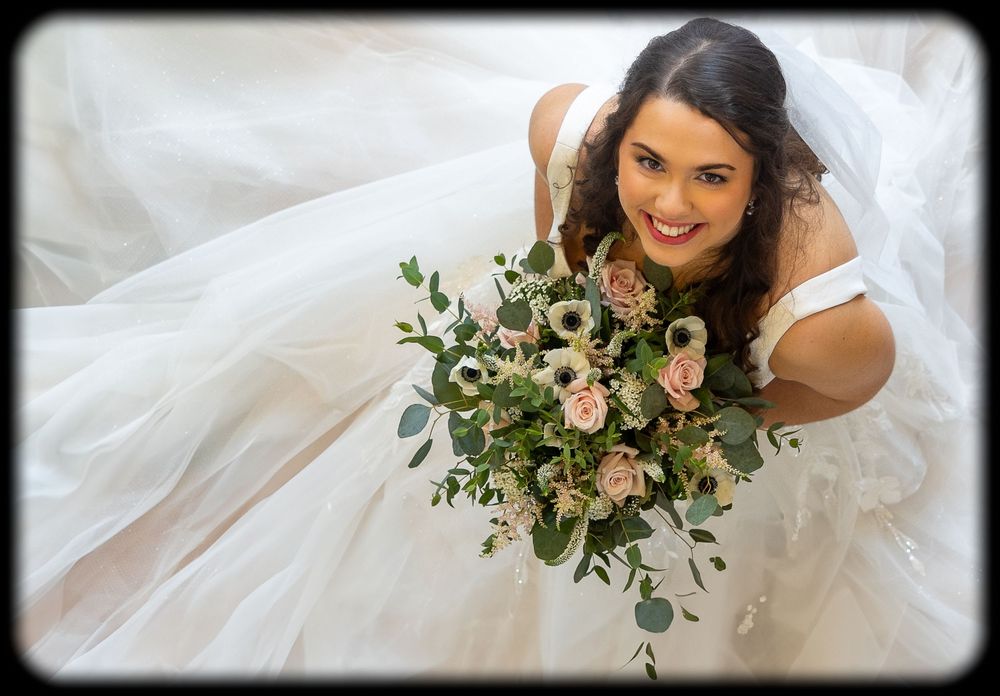 Bride in white wedding dress holding floral bouquet poses with soft natural lighting in elegant bridal portrait series.