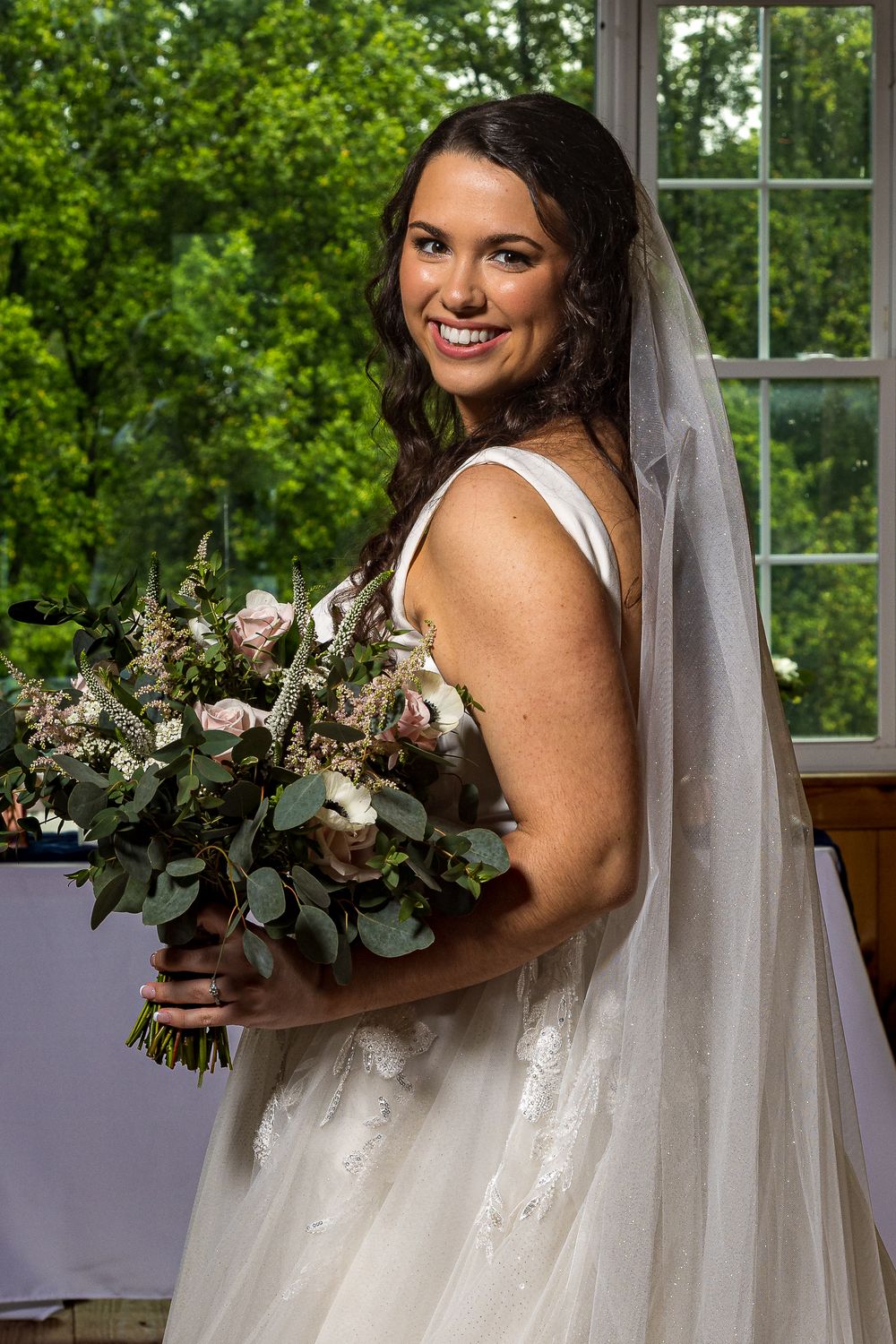 A bride in a sparkling white wedding dress holds a romantic bouquet of blush and cream flowers with eucalyptus greenery.
