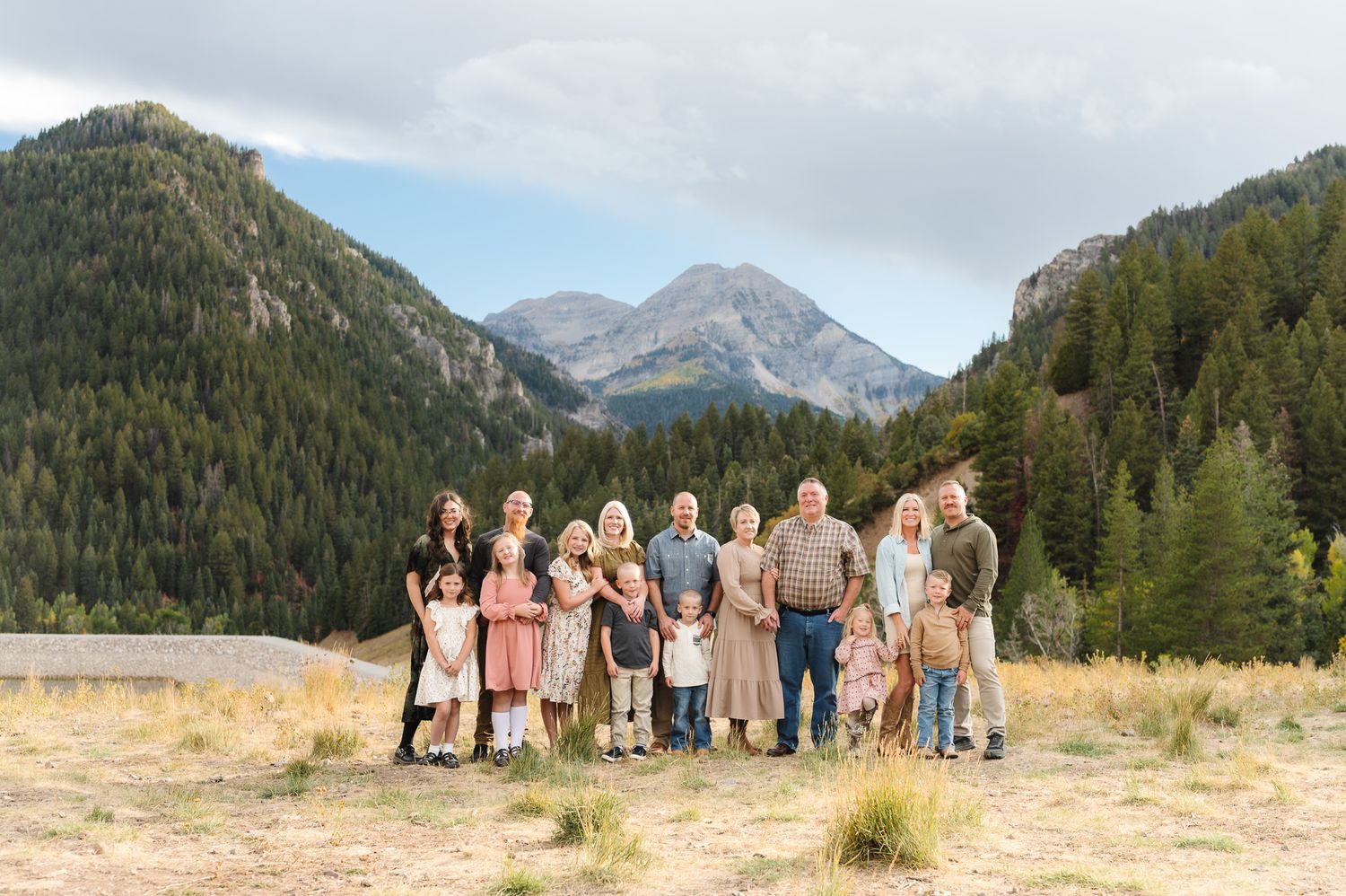 A group of people stand together in a row against a scenic mountain landscape backdrop with evergreen trees.