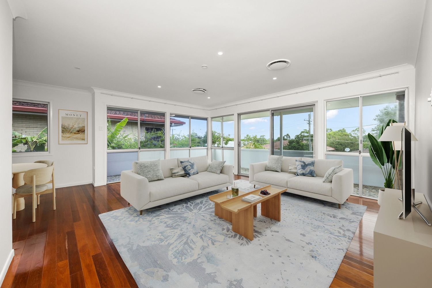 Bright spacious living room with polished hardwood floors, dual sofas, timber coffee tables, and panoramic wraparound windows.