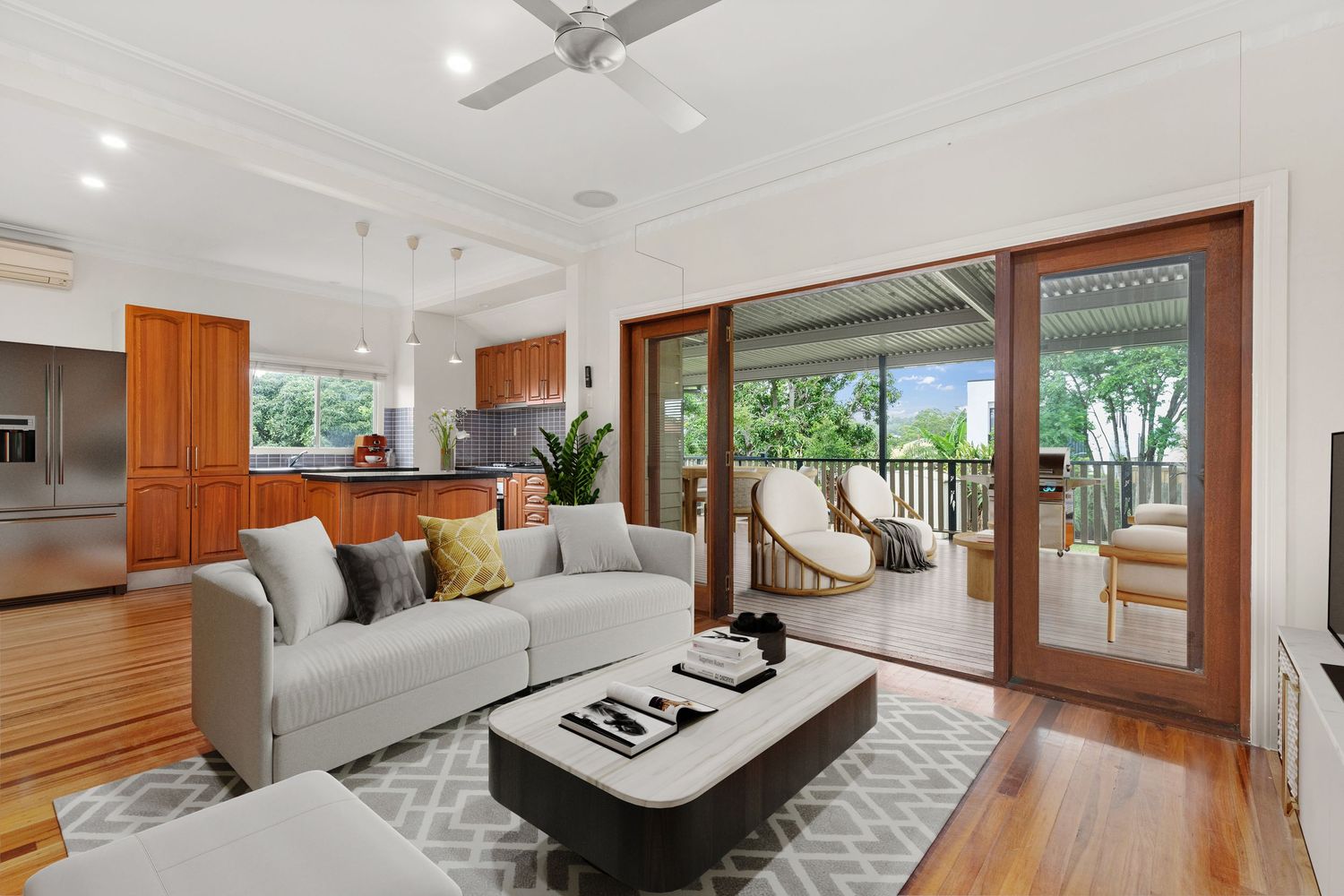 Elegant living room with timber floors, grey sofa, open kitchen, and sliding doors to a lush verandah.