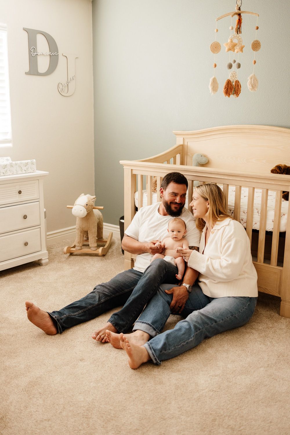 A couple and their baby relaxes on the floor of a nursery in front of their baby's crib at their in-home newborn session in San Jose, CA