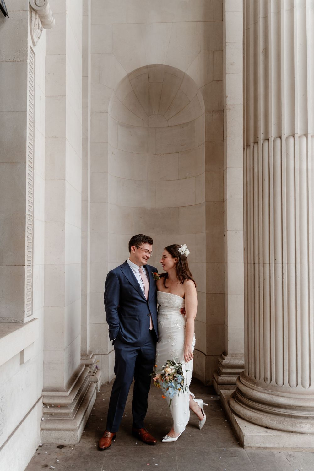 Wedding couple sharing an intimate moment between classical stone columns.