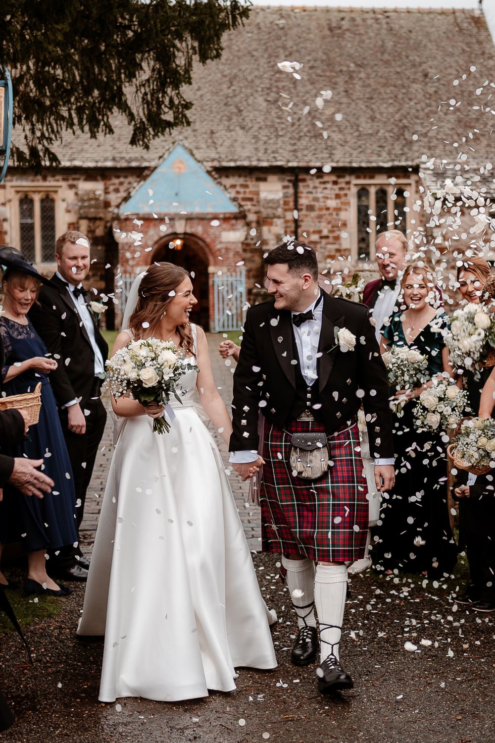 Wedding celebration with confetti shower and Scottish kilts in brick courtyard.
