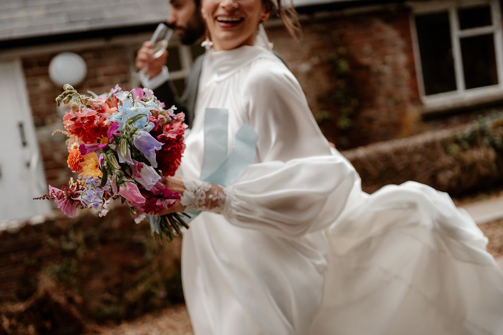 A flowing white wedding dress and colorful bouquet captured in motion against a brick building.