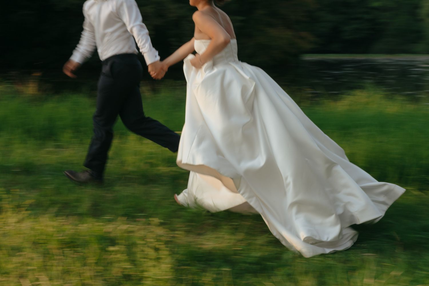 A couple in wedding attire runs playfully through a lush green garden, creating a joyful and romantic scene.