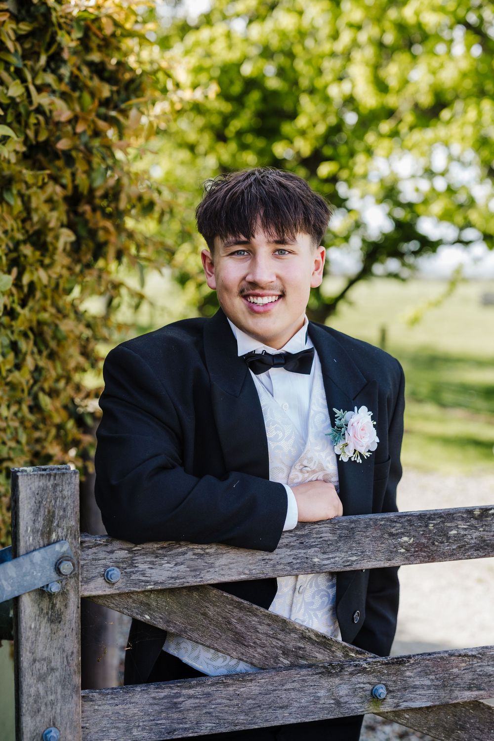 A sequence of formal portraits showing someone in a tuxedo leaning on a rustic wooden fence outdoors.