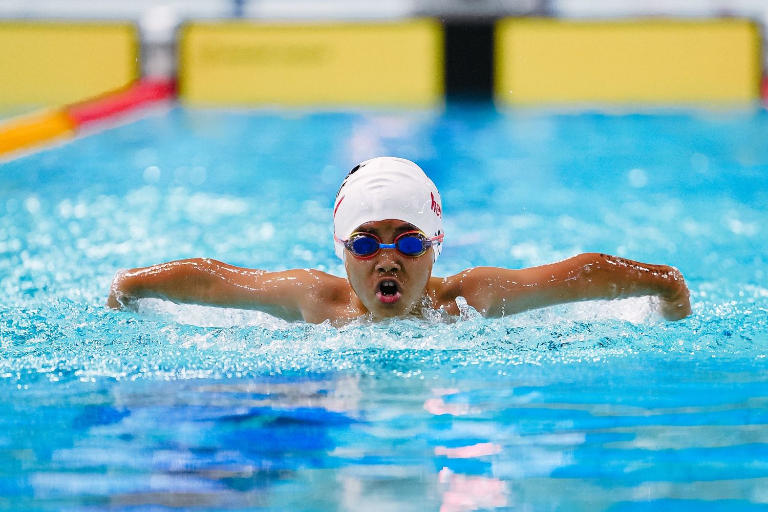 Competitive swimmers race in multiple lanes of a swimming pool during a butterfly stroke competition.