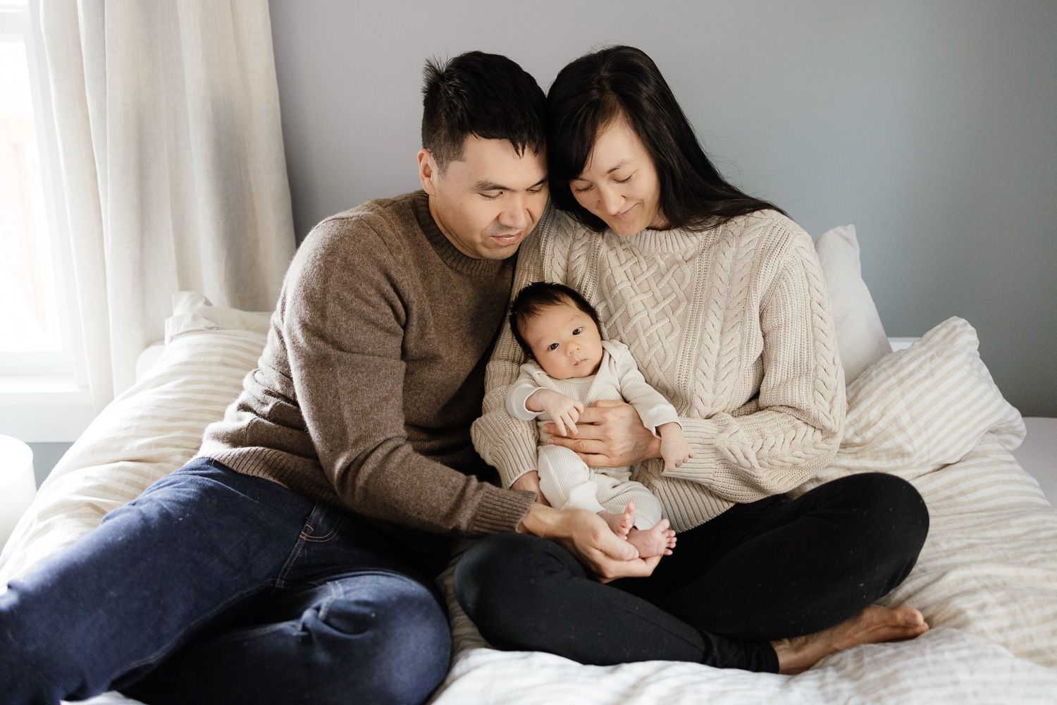 A family shares tender moments together while relaxing on a white bed during their lifestyle newborn photography session