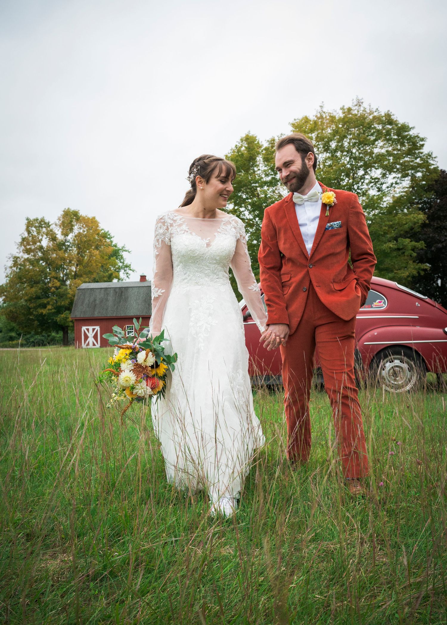 Wedding couple poses in a rustic field with a vintage red truck in the background as fall foliage sets the scene.