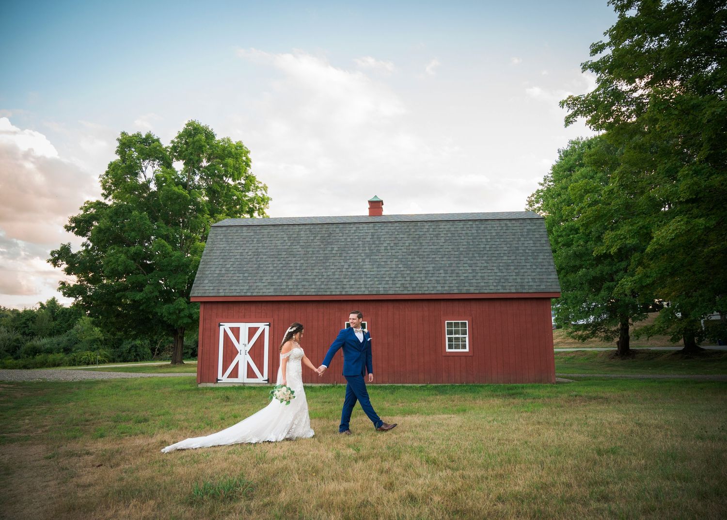 A joyful wedding couple embraces against a dark wall, with the bride holding a vibrant peach and yellow bouquet.