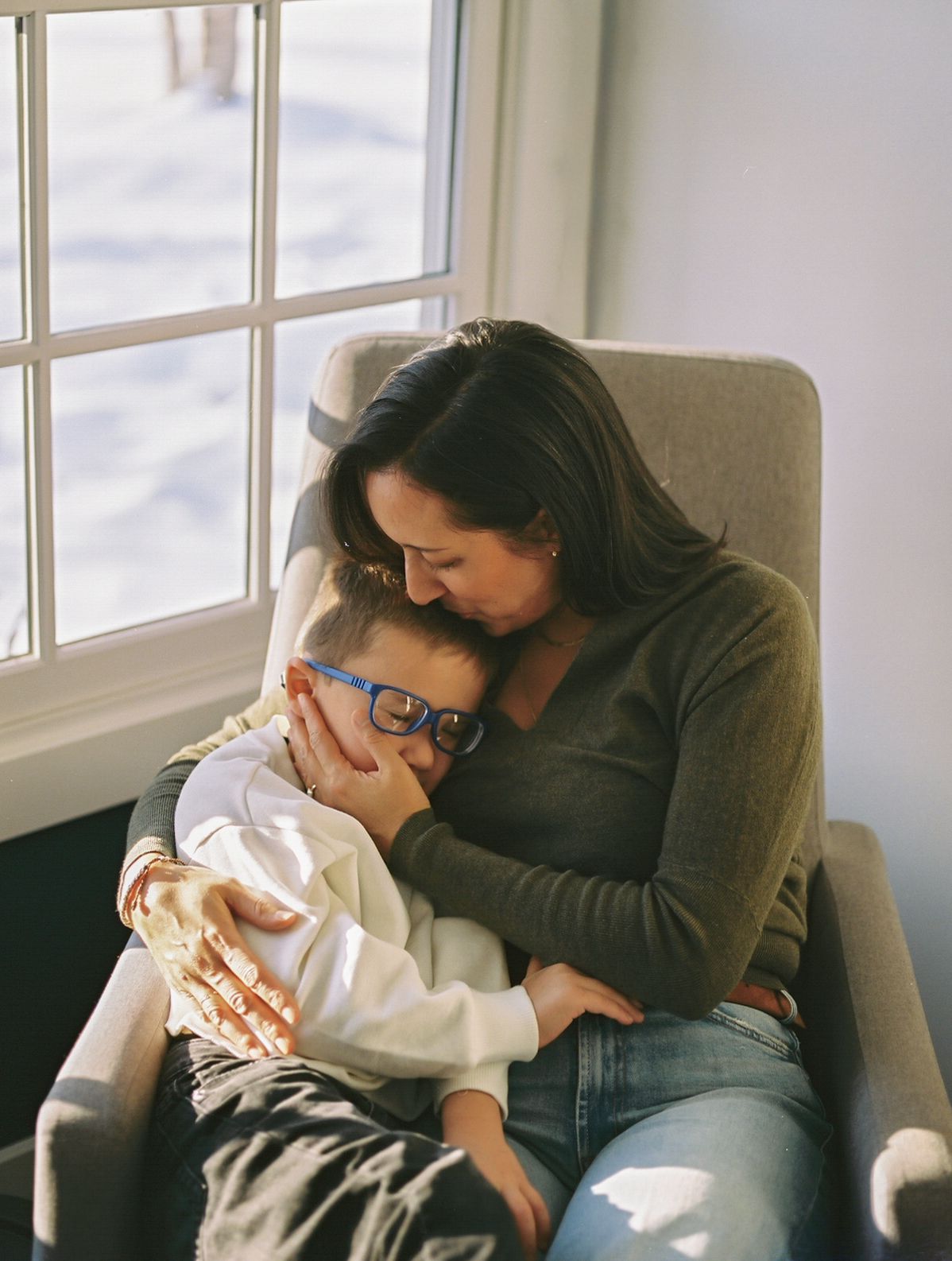 A mother snuggles with her son on a gray chair while Lauren Marie photography captures the moment on film in Middletown, NJ.