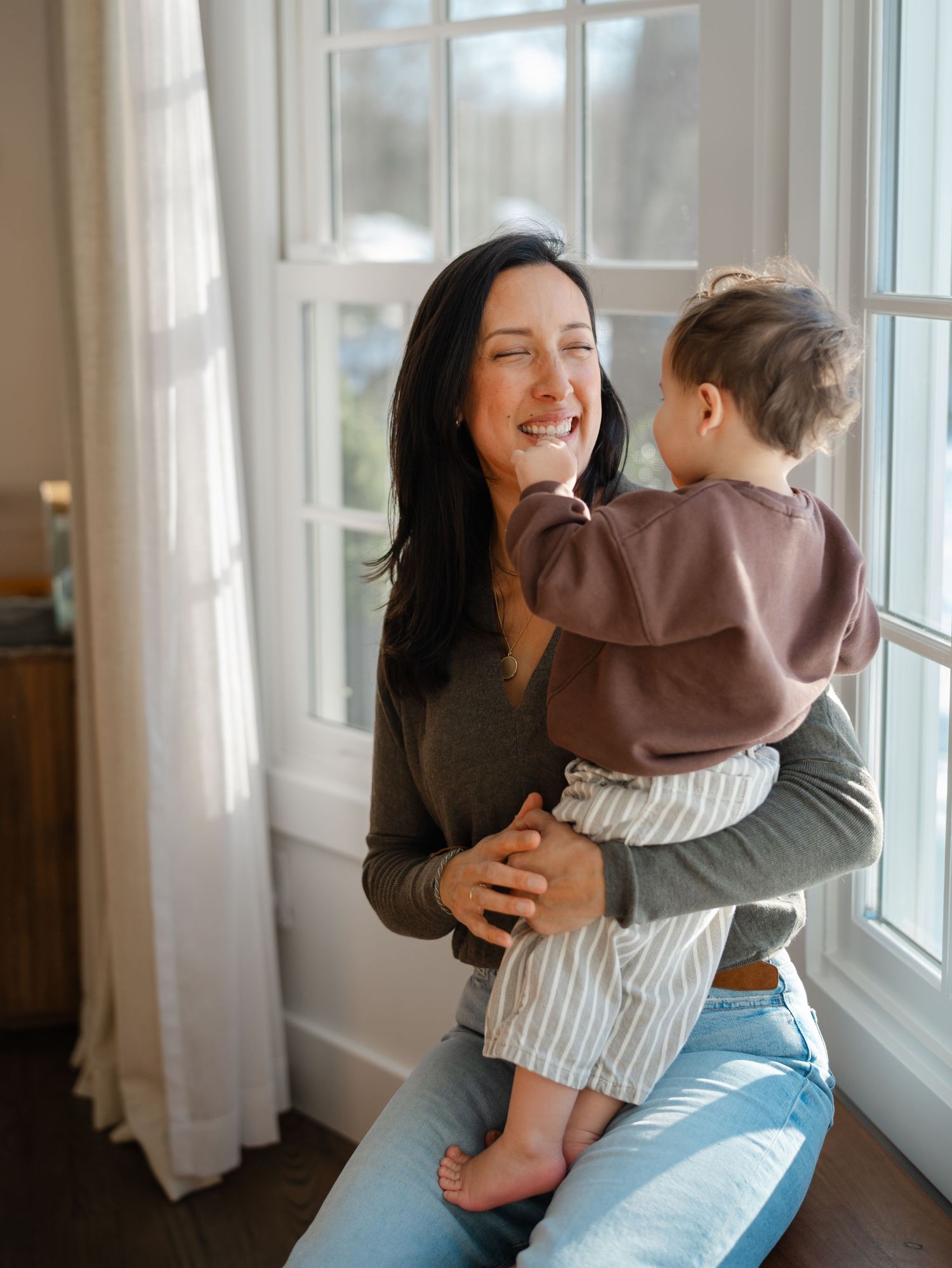 Close-up of mother holding baby on window ledge during in-home newborn and family session in Monmouth County NJ.