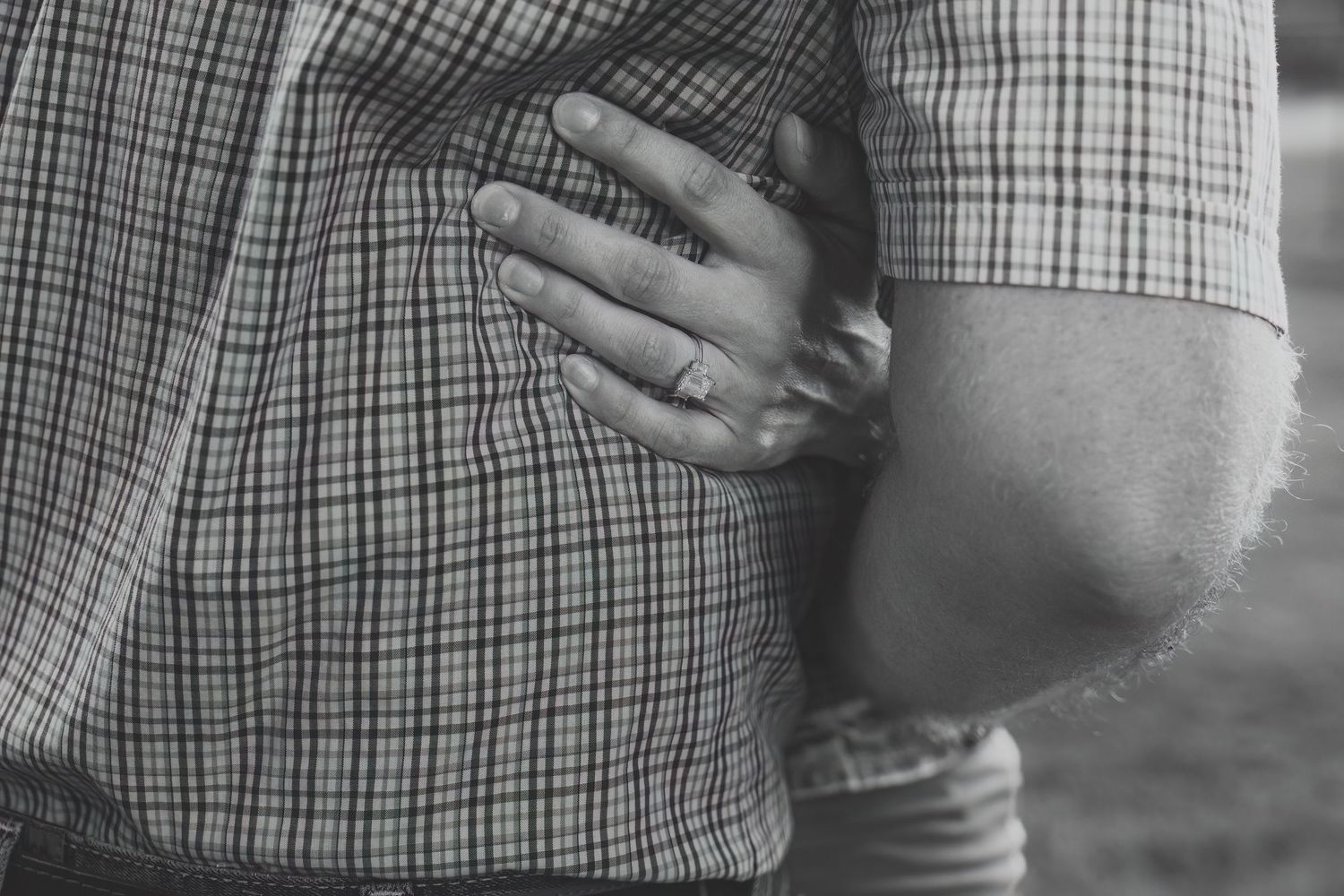 Close-up black and white photo showing hands embracing over a plaid shirt pattern.