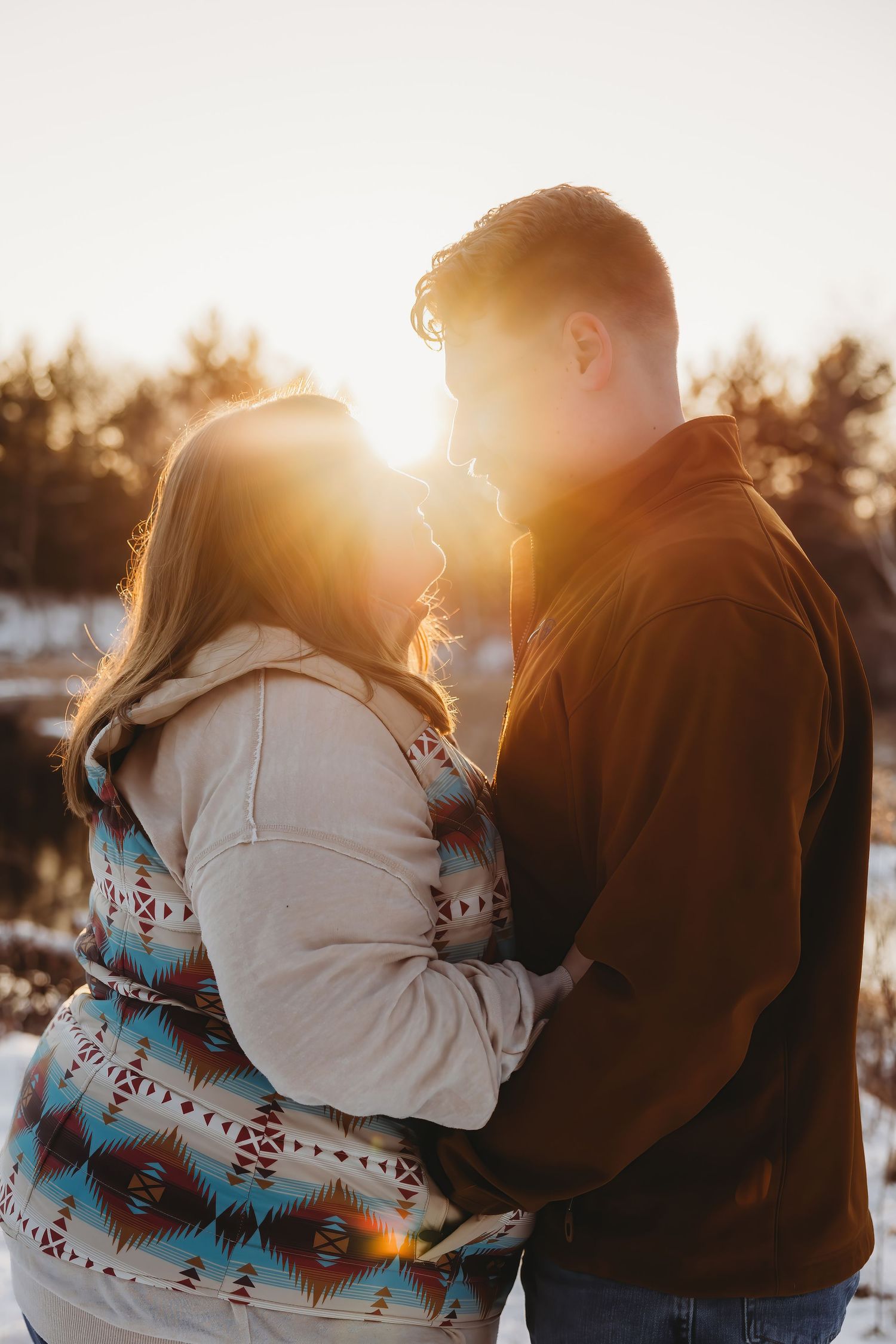 A couple embraces in warm sunset light while wearing a southwestern patterned blanket on a winter evening.