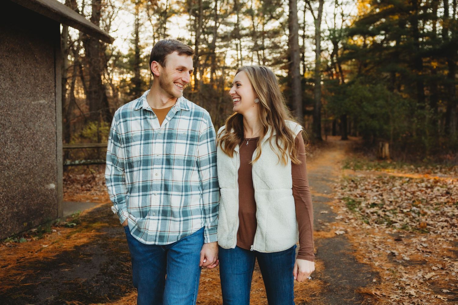 A couple walks hand in hand through a forest path during golden autumn sunset.