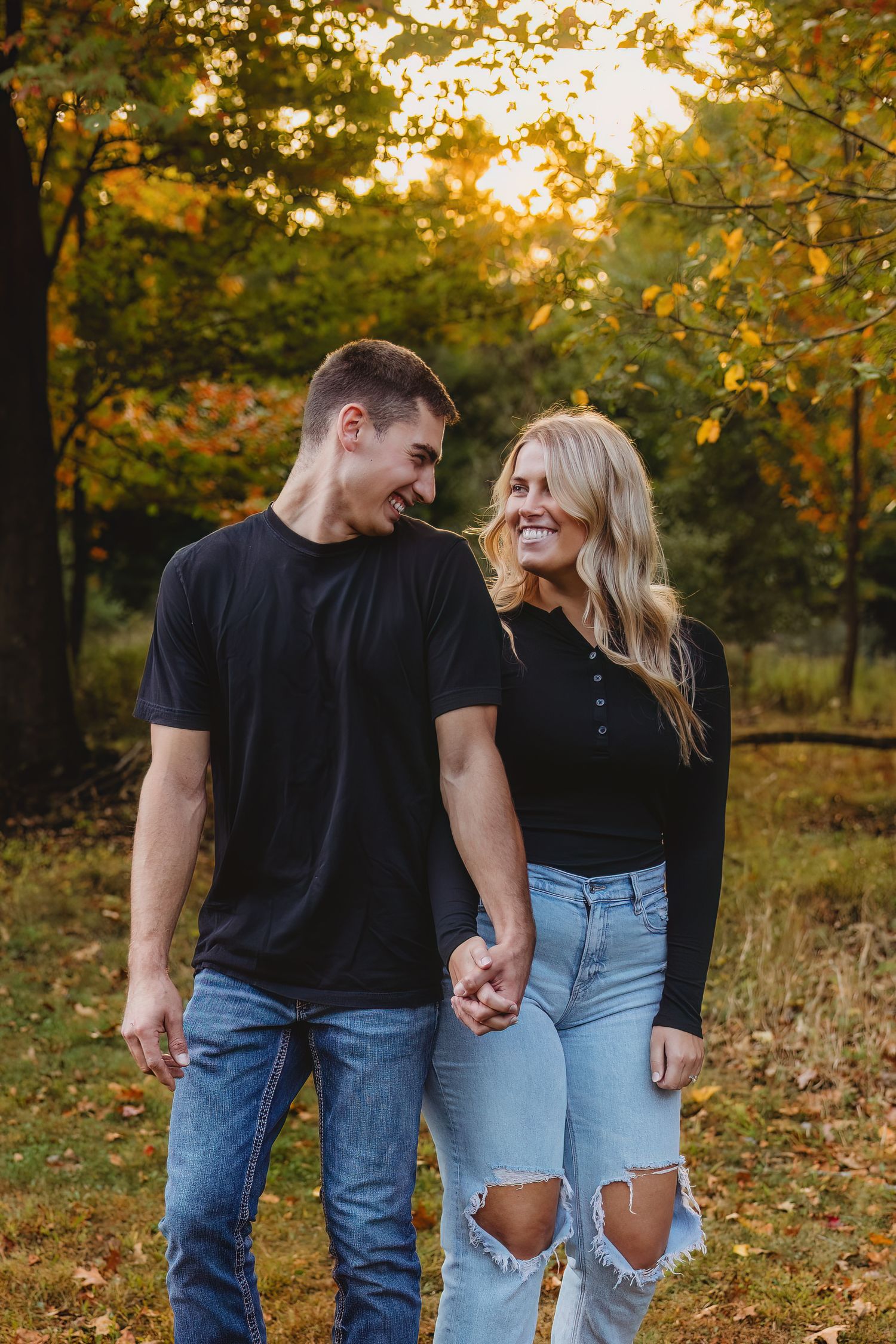 A couple in casual denim outfits share intimate moments while walking through a golden autumn forest at sunset.