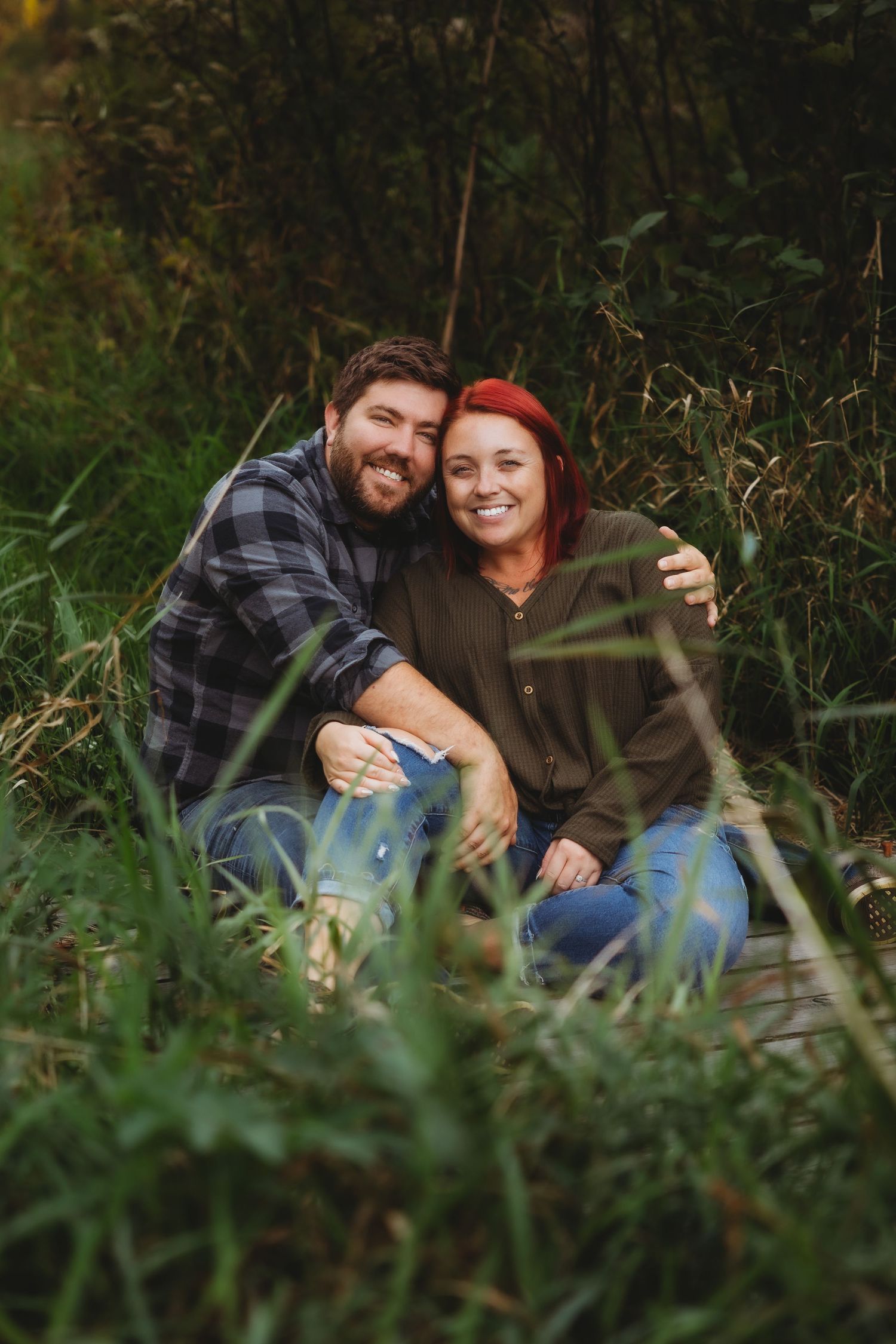 A couple shares intimate moments while sitting together in tall grass during an outdoor photo session.
