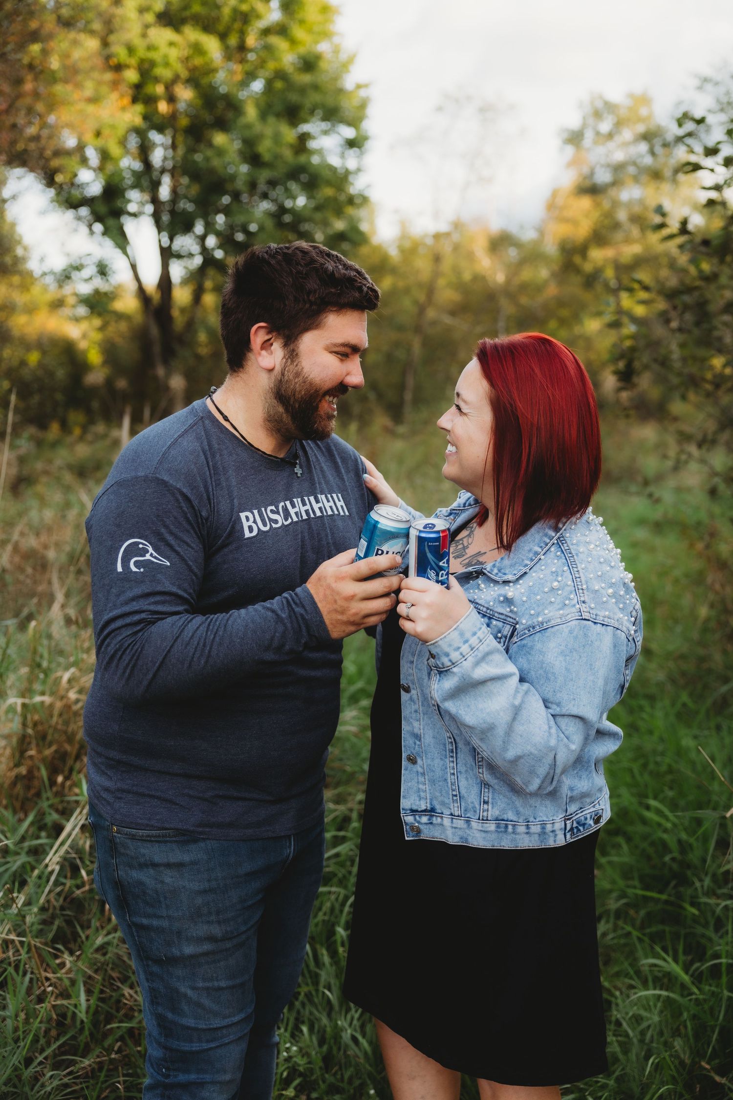 A couple shares an intimate moment in tall grass while holding blue cans during an outdoor photo session.