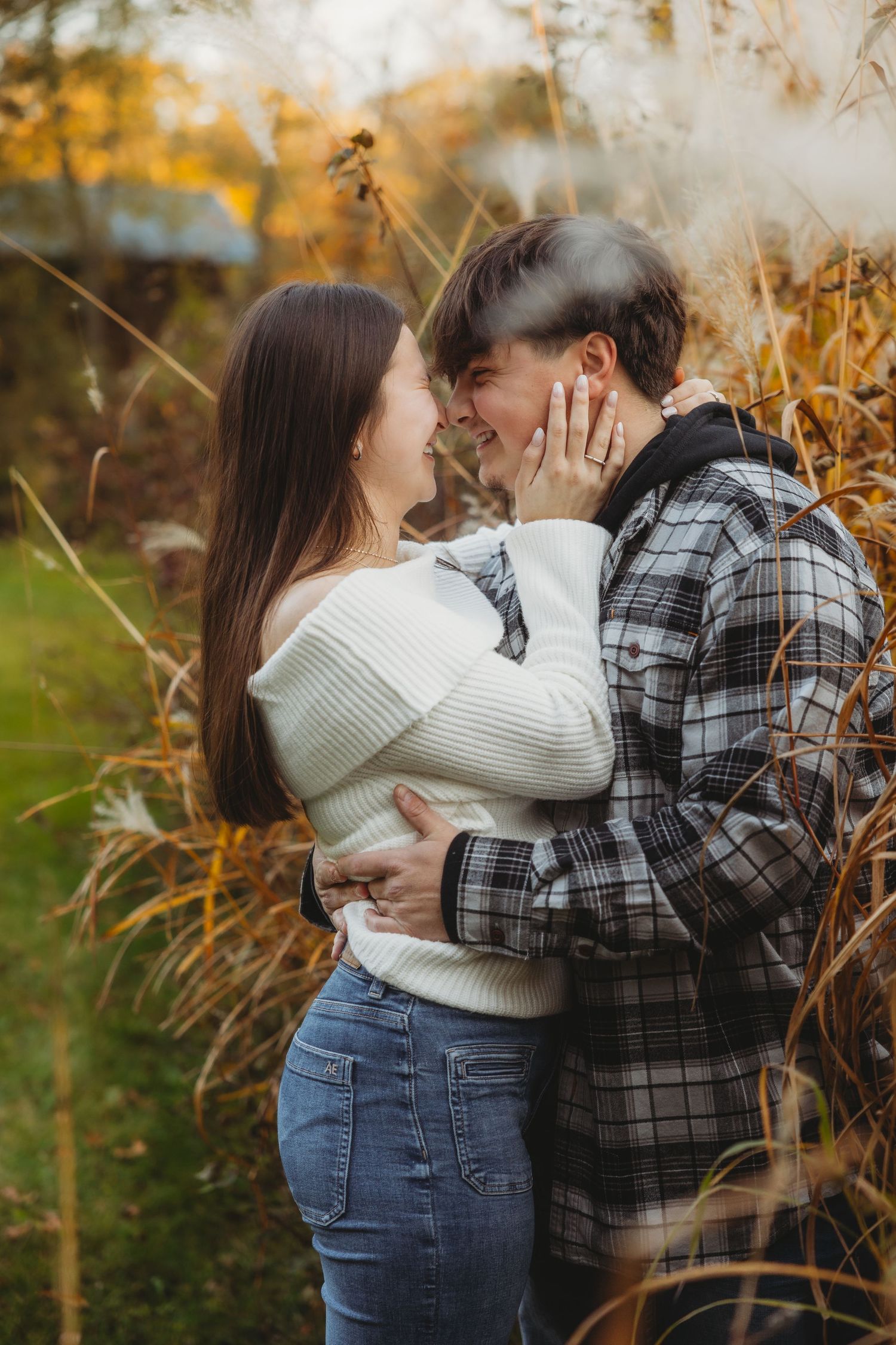 A romantic autumn moment between a couple embracing in tall grass with golden fall colors in the background.