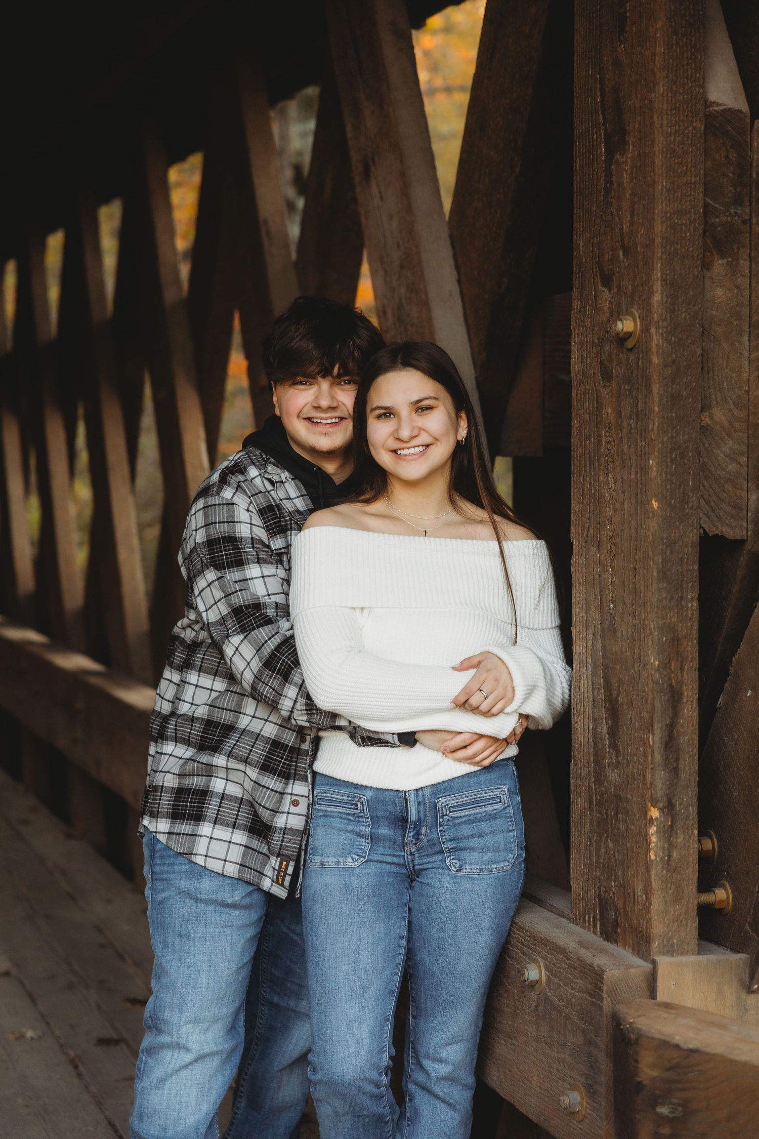 Two people wearing matching outfits with jeans and plaid shirts stand close together in a wooden walkway.